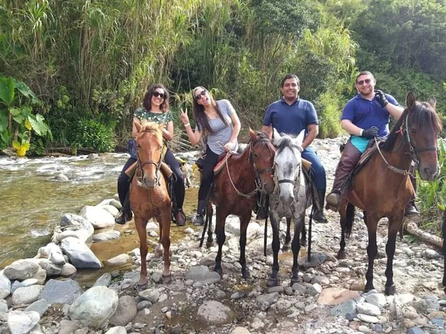 Four people horseback riding through a shallow rocky river crossing