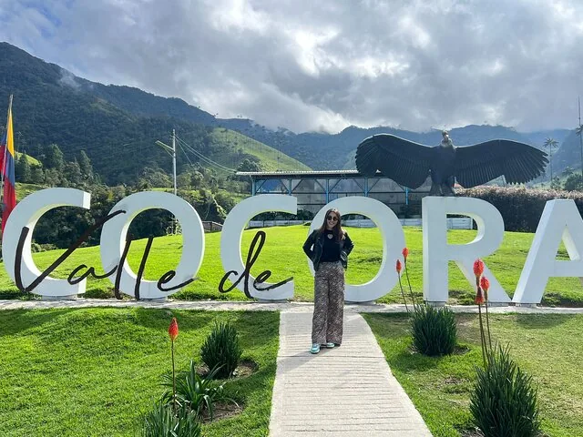 Frau steht vor einem großen Cocora-Schild mit Bergkulisse im Hintergrund
